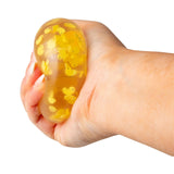 Hand squeezing a clear yellow duck squish ball showing it bulging with duck clay slices visible inside