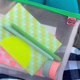 Mesh pouch with colorful items including a green pen, a notebook, and patterned paper.