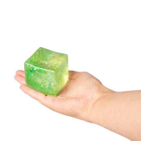 Green glitter sugar cube resting in an open palm showing its cube shape and sparkly gel interior