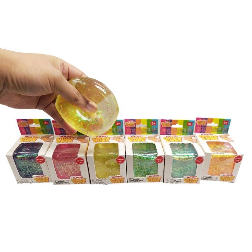 Hand holding a colorful slime above shelves with variously colored slimes in boxes.