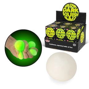 Hand squeezing a glowing green squish ball in the dark alongside product display box and daylight ball