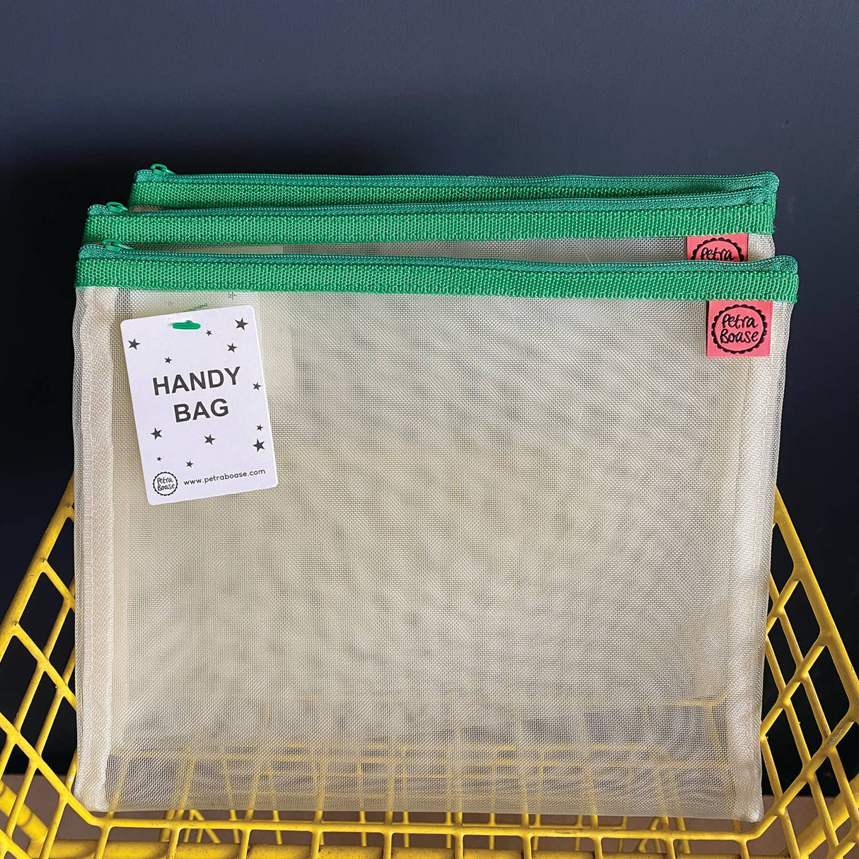 Three mesh bags with green zippers on a yellow basket against a dark background