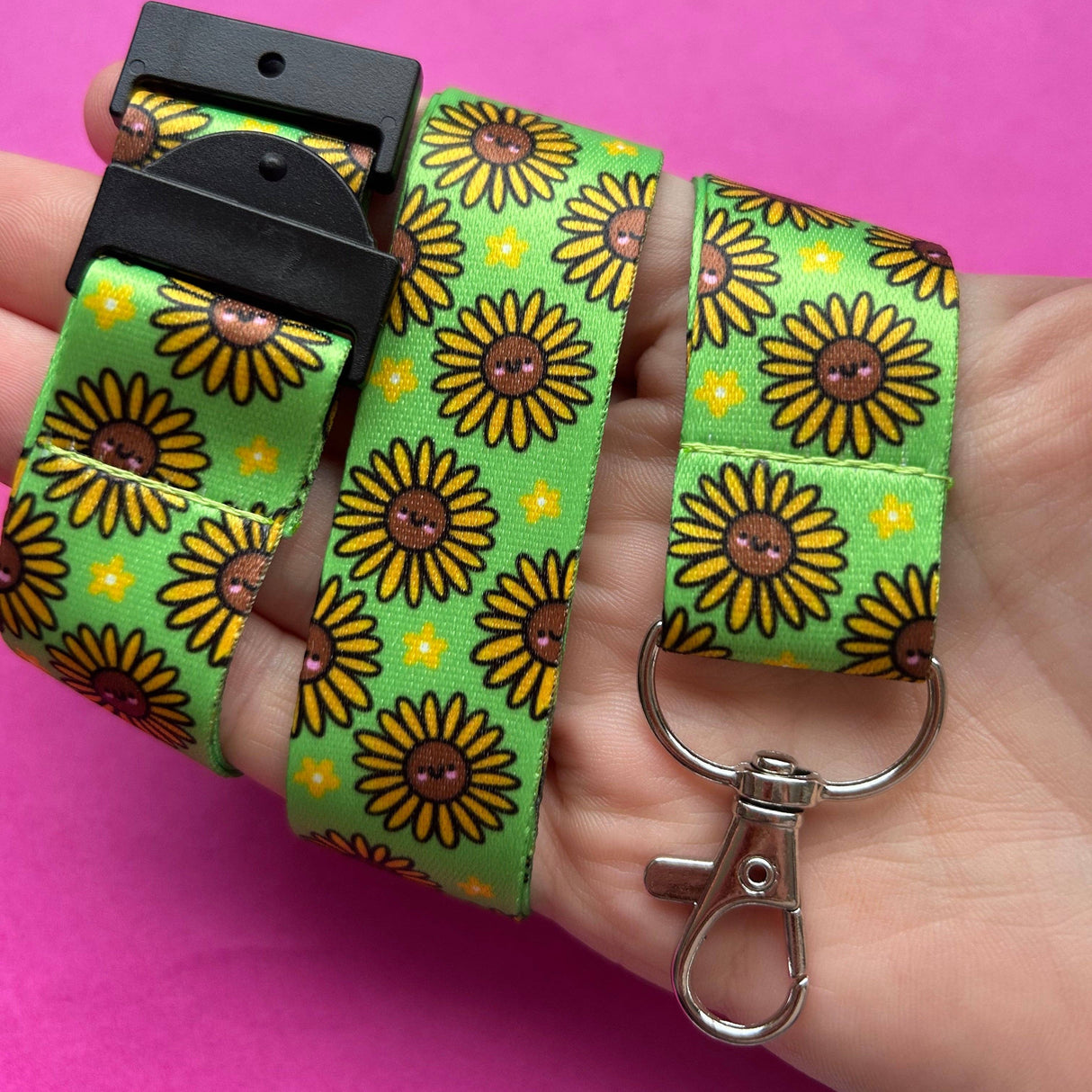 Adult hand holding the Happy Sunflowers kawaii lanyard looped around wrist showing safety breakaway clasp and swivel clip with full sunflower print