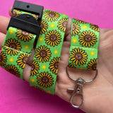 Adult hand holding the Happy Sunflowers kawaii lanyard looped around wrist showing safety breakaway clasp and swivel clip with full sunflower print