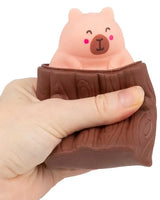 Hand squeezing brown log squeeze toy with kawaii pink capybara popping up from inside