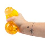 Tattooed hand squeezing a transparent orange honey bee squish ball showing gel oozing through the honeycomb outer shell