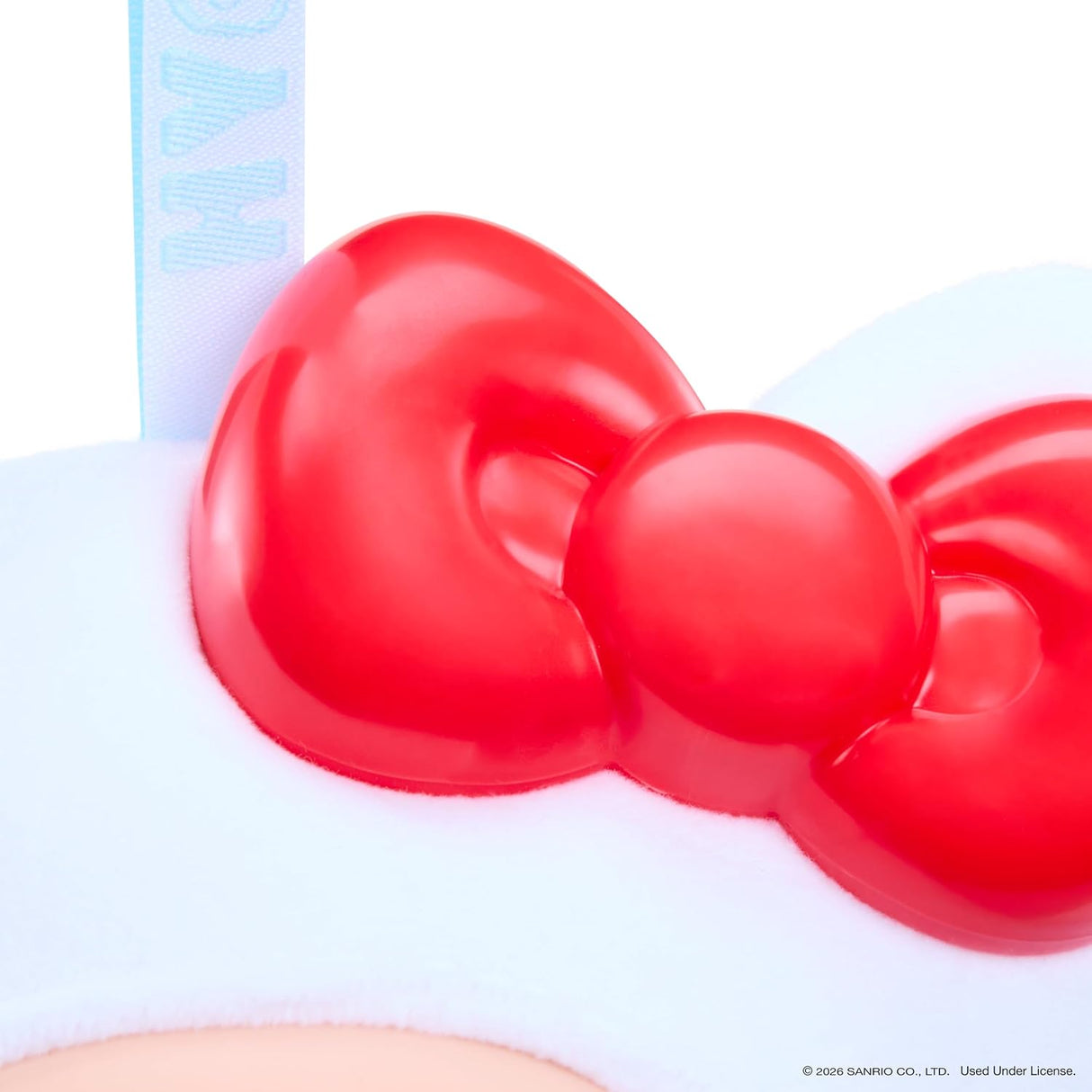 Close-up of a red Hello Kitty bow on a white headband with a light blue ribbon, with a small portion of a peach-colored face visible at the bottom.