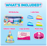 An included items overview graphic for a Jelly Cakes toy set on a light blue background, with the headline 'WHAT'S INCLUDED?'. The image shows the gift box, four jelly cake slices, a collector's manual, four bags of sprinkles, and a pink mystery ring.
