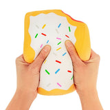 Two hands squeezing a jumbo golden yellow squishy Pop-Tart with white icing and rainbow sprinkles