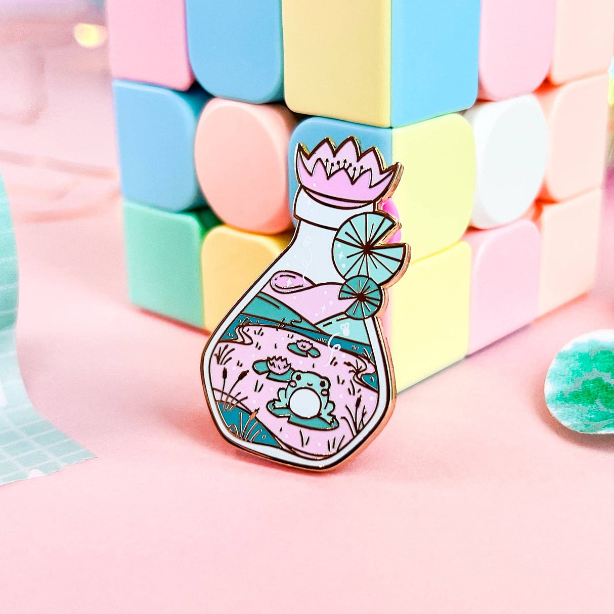 Lula Rocks Bottled Frog UV Glow enamel pin standing, pastel blocks lifestyle shot