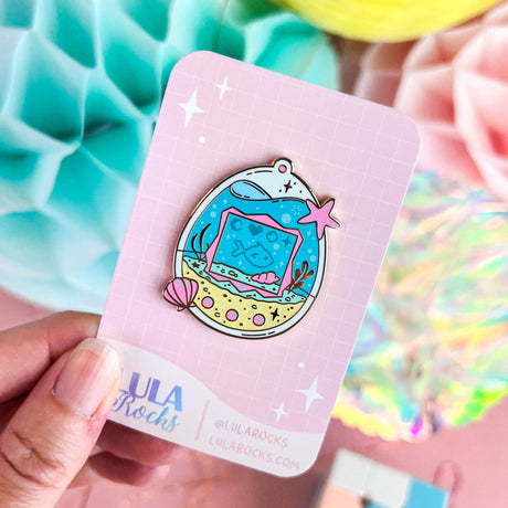 Lula Rocks Digital Aquarium enamel pin on pink backing card, pastel lifestyle shot