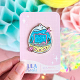 Colorful enamel pin on a pink card with 'Lula Rocks' branding, held against a vibrant background.
