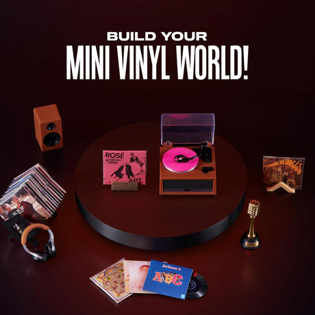 Mini record player with pink vinyl surrounded by miniature headphones, speaker and album sleeves