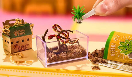 Miniature desert terrarium habitat being assembled with snake figure, sand and plant accessories
