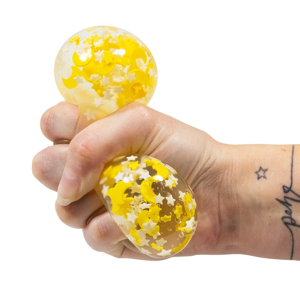 Moons and Stars glow in the dark squish ball being squeezed in a hand, showing the transparent gel interior with moon and star confetti visible through the stretched skin