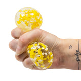 Moons and Stars glow in the dark squish ball being squeezed in a hand, showing the transparent gel interior with moon and star confetti visible through the stretched skin