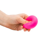 Adult hand squeezing a hot pink neon squish ball, showing its soft and stretchy texture