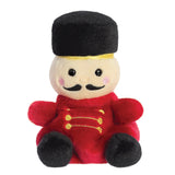 Palm Pals Marius Nutcracker plush, a small palm-sized stuffed nutcracker soldier with a cream face, black embroidered moustache, a tall black hat with gold band, a red uniform with gold embroidered detail, and black feet