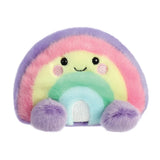 Aurora Palm Pals Vivi Rainbow plush — a pastel rainbow soft toy with bands of purple, pink, yellow, green, and blue, a silvery embroidered base detail, pink blush cheeks, and a smiling face