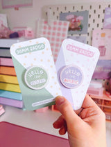 Peachy Lane Studio Hello I Am Autistic badge green and lilac variants held, studio background