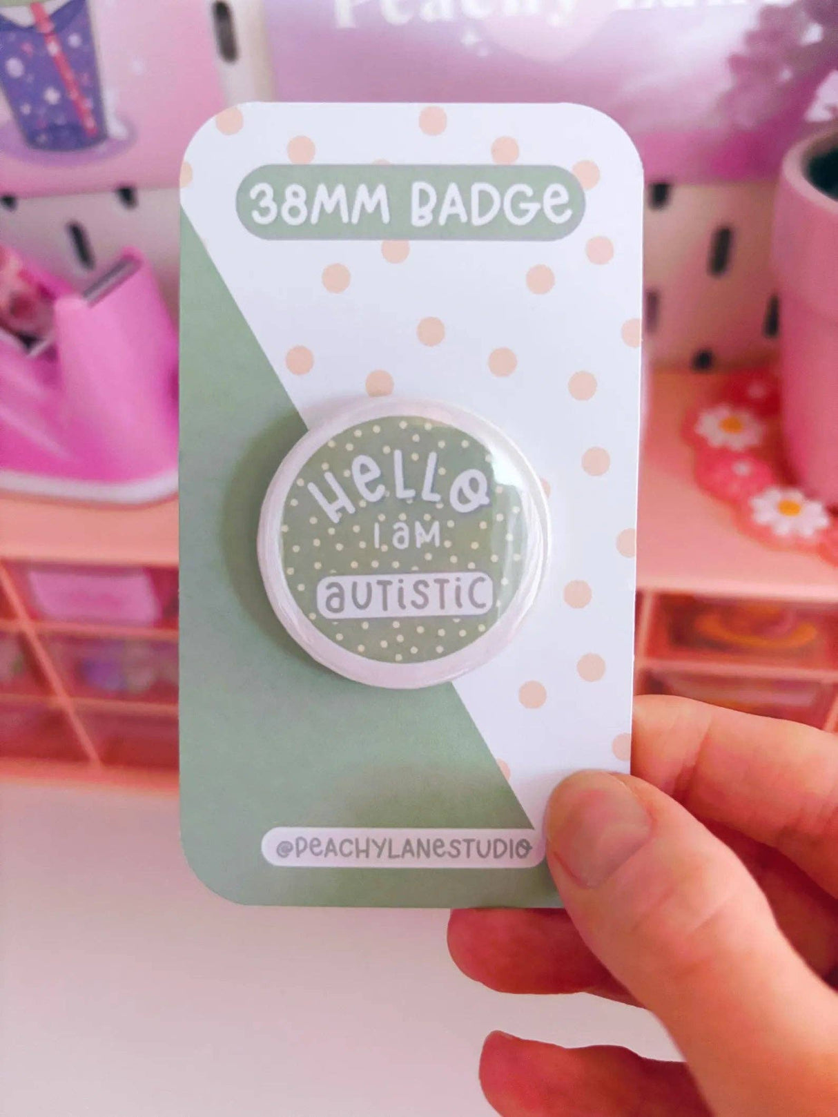 Peachy Lane Studio Hello I Am Autistic 38mm badge held in hand, sage green