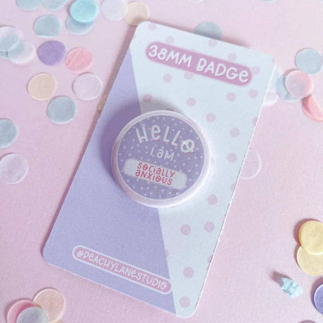 Peachy Lane Studio Hello I Am Socially Anxious badge, lilac, flat lay with pastel confetti