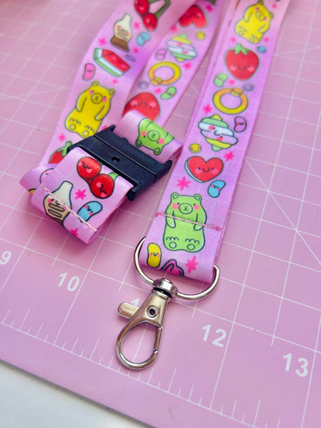 Pick 'n' Mix kawaii lanyard laid flat on a pink mat showing the safety breakaway clasp and metal swivel clip with full print visible