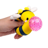 Hand squeezing a yellow striped plush bee Queasy Squeezie causing pink water bead nose to bulge out