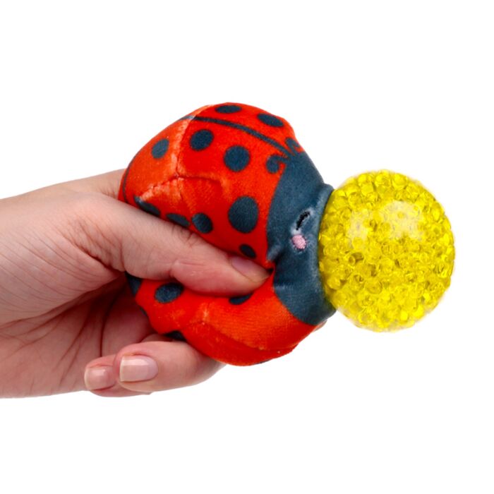 Hand squeezing a red plush ladybird Queasy Squeezie causing yellow water bead nose to bulge out