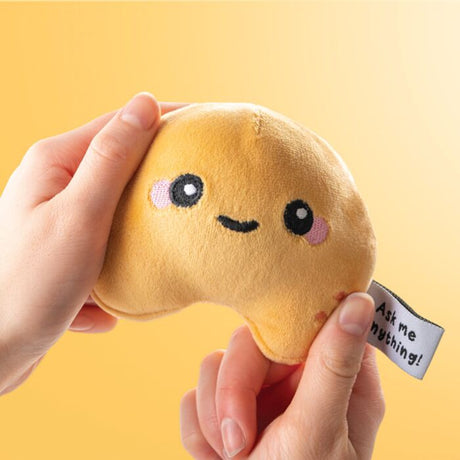 Queasy Squeezies fortune teller cookie sensory plush held in hands, yellow background
