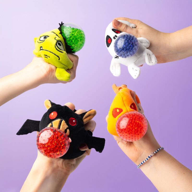 Four hands each squeezing a different Queasy Squeezies Halloween plush toy showing the coloured gel bead centres