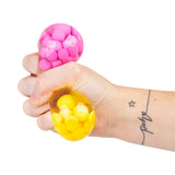 Hand squeezing a pink and yellow Scrunchems ASMR squish ball showing the bead texture