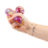 Hand squeezing a Scrunchems Happy Little Squish Ball filled with colourful smiley beads