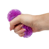 Hand squeezing a purple Scrunchems Ombre Sensory Sugar Ball puffer toy on a teal background