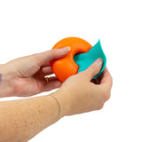Two hands peeling the stretchy teal icing topper off an orange squishy donut fidget toy