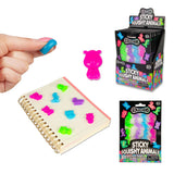 Sticky squishy animal figures stuck to a notebook alongside retail pack and display box, with finger holding blue figure