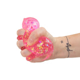 Hand squeezing a pink holographic glitter Scrunchems Sugar Diamond squishy, deforming its shape
