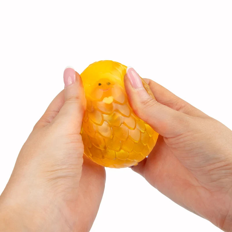 Hands squeezing orange Scrunchems Sugar Dragon Egg revealing dragon face inside shell