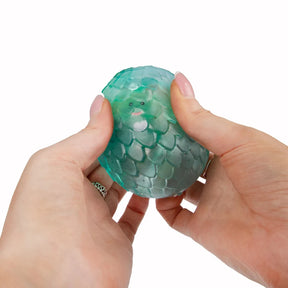 Hands squeezing teal Scrunchems Sugar Dragon Egg showing translucent scale texture