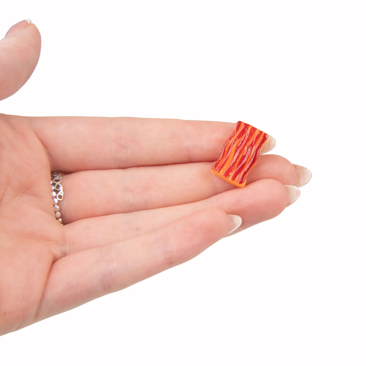 Close-up of a tiny sticky bacon rasher accessory resting on an open palm, showing detail and scale
