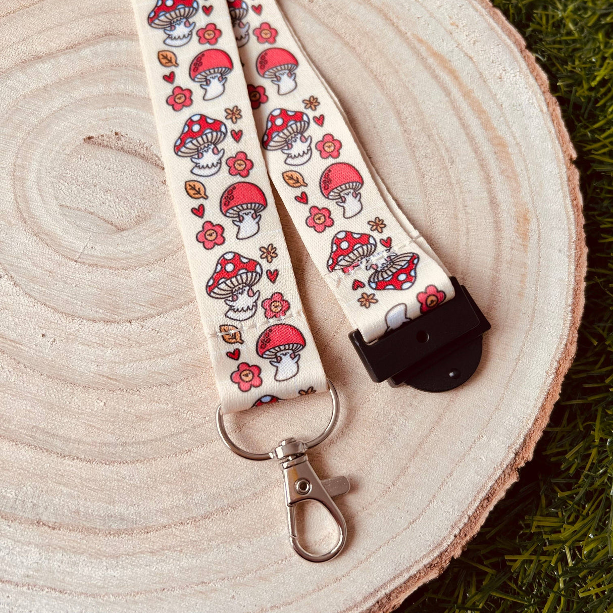 Shroom Cuties lanyard laid on a wooden slice at an angle showing the breakaway clasp end and full cottagecore mushroom print