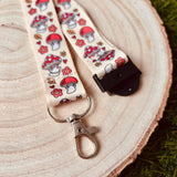 Shroom Cuties kawaii mushroom lanyard laid flat on a wooden slice showing full red toadstool and floral print with breakaway clasp and swivel clip