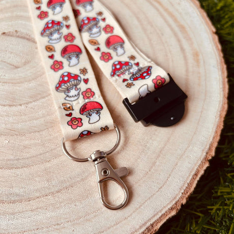 Shroom Cuties kawaii mushroom lanyard laid flat on a wooden slice showing full red toadstool and floral print with breakaway clasp and swivel clip