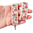 Adult hand holding the Shroom Cuties kawaii lanyard on a white background showing the full cream base mushroom and floral print with swivel clip