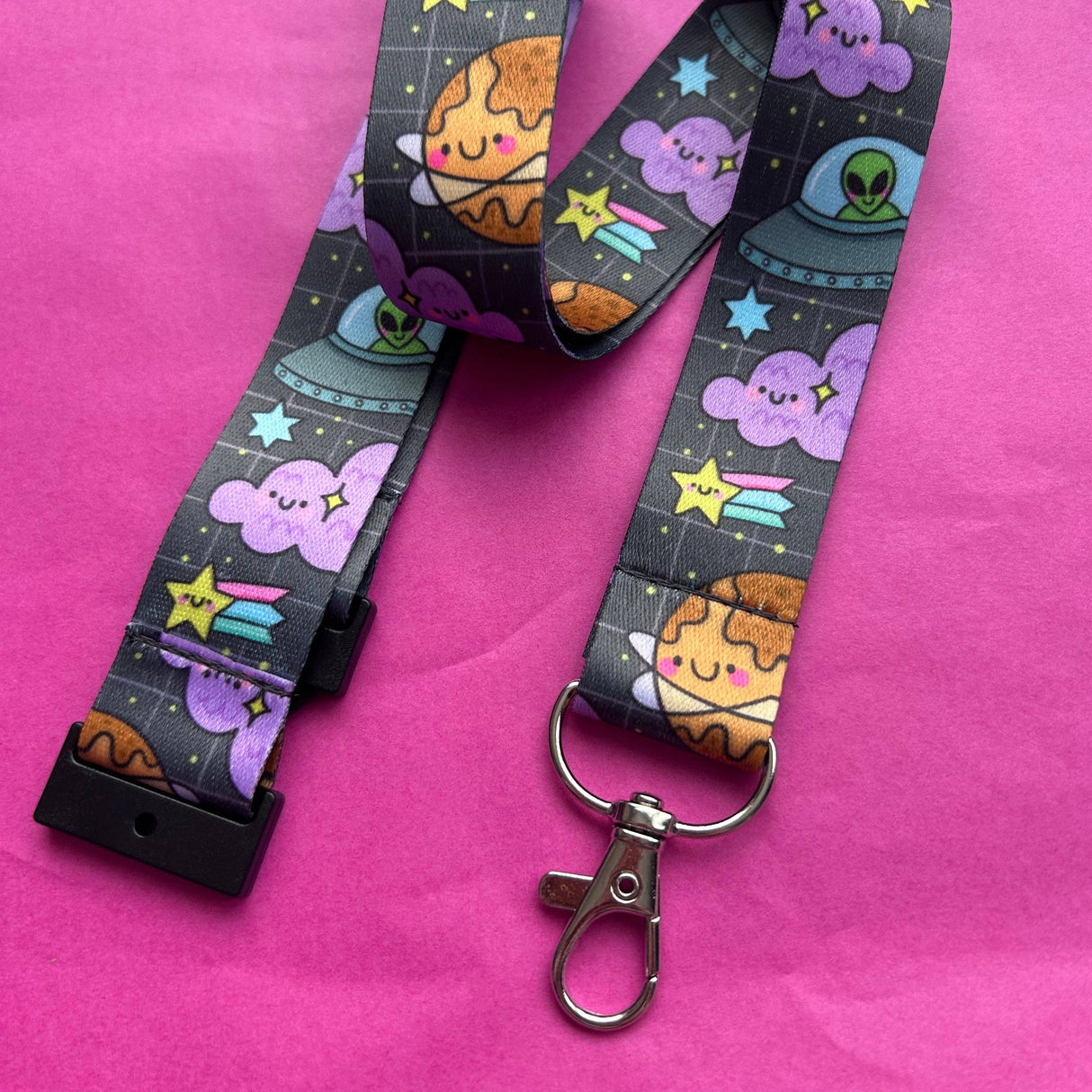 Full length Space Cuties kawaii lanyard laid out on a pink background showing the full space print with planets, aliens, stars and clouds
