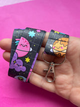 Space Cuties lanyard looped in an adult palm showing kawaii planet and alien print detail with metal clip