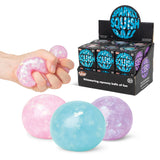 Three Scrunchems Sparkly Squish Balls in pink, blue, and purple shown with one being squeezed in a hand alongside retail display box