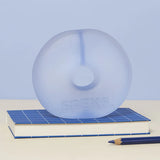 Periwinkle blue translucent Speks Gump Jumbo Loop standing upright on a desk beside a notebook