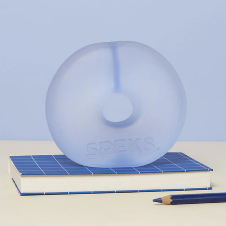 Periwinkle blue translucent Speks Gump Jumbo Loop standing upright on a desk beside a notebook