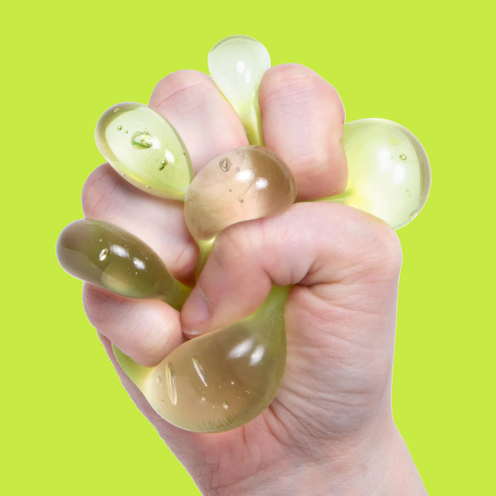 Fist fully squeezing a bright yellow-green Algae Speks Gump Original, gel oozing between fingers against a green background